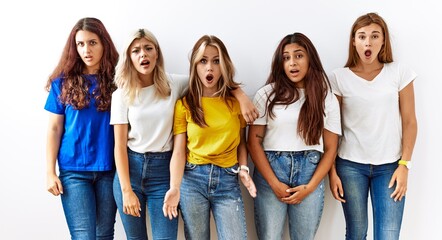 Group of young girl friends standing together over isolated background in shock face, looking skeptical and sarcastic, surprised with open mouth