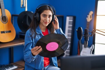 Young hispanic girl artist listening to music holding vinyl disc at music studio