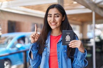 Young teenager girl holding canada passport smiling with an idea or question pointing finger with happy face, number one