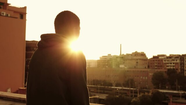 Lonely african man on the roof looking the sunset over the city- back view