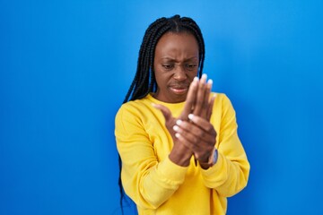 Beautiful black woman standing over blue background suffering pain on hands and fingers, arthritis inflammation