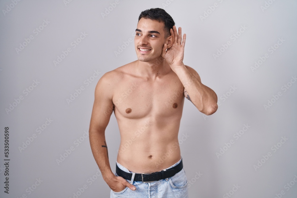 Poster Handsome hispanic man standing shirtless smiling with hand over ear listening an hearing to rumor or gossip. deafness concept.