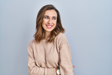 Obraz premium Young woman standing over isolated background looking away to side with smile on face, natural expression. laughing confident.