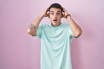 Handsome hispanic man standing over pink background crazy and scared with hands on head, afraid and surprised of shock with open mouth