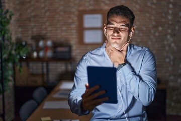 Handsome hispanic man working at the office at night touching painful neck, sore throat for flu, clod and infection