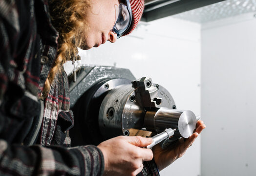 Industrial woman machinist uses a CNC lathe machine and a micrometer for calibration	