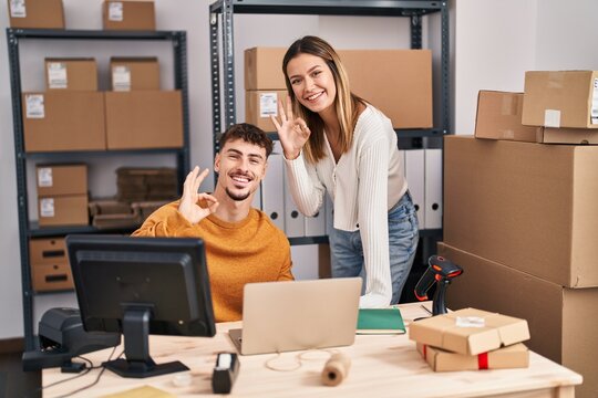 Young couple working at small business ecommerce doing ok sign with fingers, smiling friendly gesturing excellent symbol
