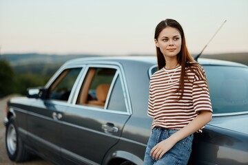 A woman driver near her retro car relaxing from the tough road and enjoying the scenery 