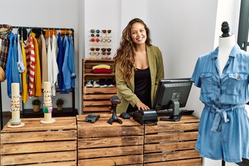 Young hispanic shopkeeper woman smiling happy working at clothing store.