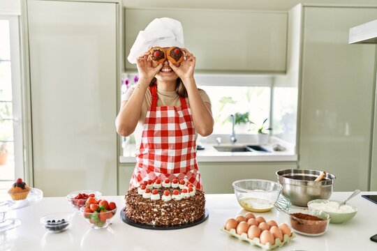 Young beautiful hispanic woman smiling confident holding cupcakes over eyes at the kitchen