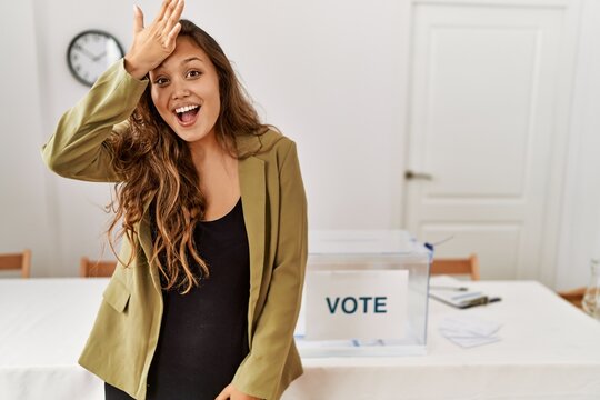 Beautiful hispanic woman standing at political campaign room surprised with hand on head for mistake, remember error. forgot, bad memory concept.