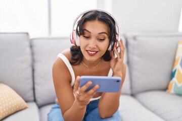 Young beautiful hispanic woman watching video on smartphone sitting on sofa at home