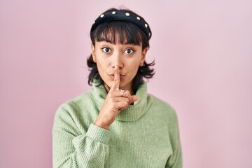 Young beautiful woman standing over pink background asking to be quiet with finger on lips. silence and secret concept.