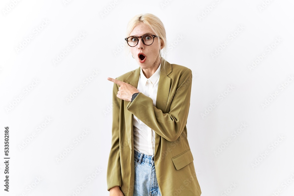 Sticker Beautiful caucasian business woman standing over isolated background surprised pointing with finger to the side, open mouth amazed expression.