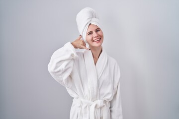 Blonde caucasian woman wearing bathrobe smiling doing phone gesture with hand and fingers like talking on the telephone. communicating concepts.