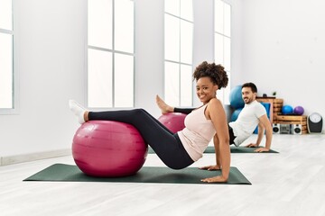 Young african american woman and hispanic man exercising at pilates room, stretching body and doing...