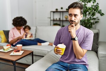Hispanic father of interracial family drinking a cup coffee thinking worried about a question, concerned and nervous with hand on chin