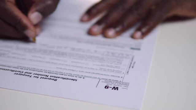Close-up of black african migrant's hand filling out W-9 Tax application form