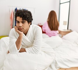 Young couple with serious expression on trouble sitting on the bed at bedroom.