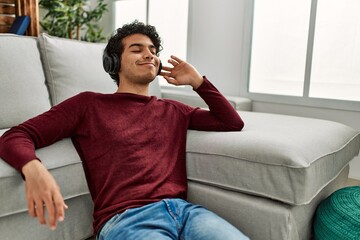 Young hispanic man listening to music sitting on the floor at home.