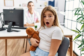 Blonde little girl at pediatrician clinic with female doctor scared and amazed with open mouth for...
