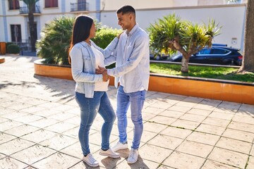 Young latin couple expecting baby standing together touching belly at park