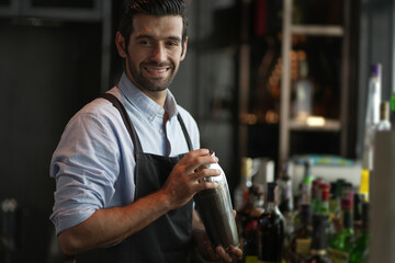 Expert barman is making cocktail at night club. handsome smiling bartender with classical metal shaker. Young handsome smiling male bartender in apron.