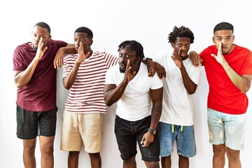 Young african group of friends standing together over isolated background hand on mouth telling secret rumor, whispering malicious talk conversation