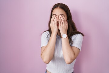 Young hispanic girl standing over pink background rubbing eyes for fatigue and headache, sleepy and...