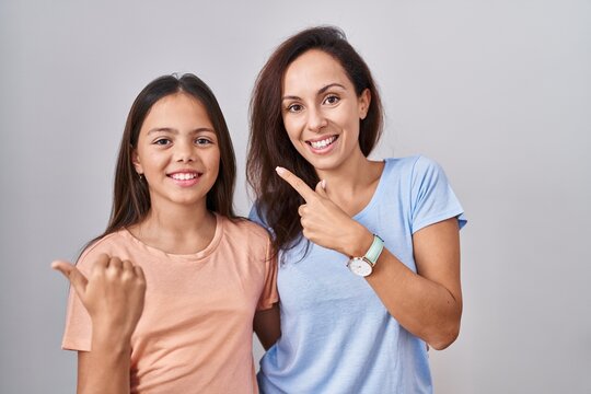 Young Mother And Daughter Standing Over White Background Cheerful With A Smile On Face Pointing With Hand And Finger Up To The Side With Happy And Natural Expression