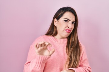 Young hispanic woman standing over pink background disgusted expression, displeased and fearful...