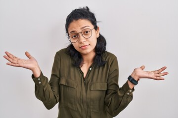 Hispanic woman with dark hair standing over isolated background clueless and confused expression...