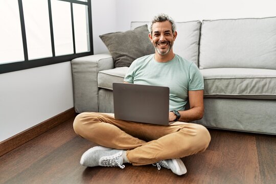 Middle age hispanic man using laptop sitting on the floor at the living room with a happy and cool smile on face. lucky person.