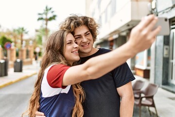 Young caucasian couple smiling happy and hugging make selfie by the smartphone at the city.