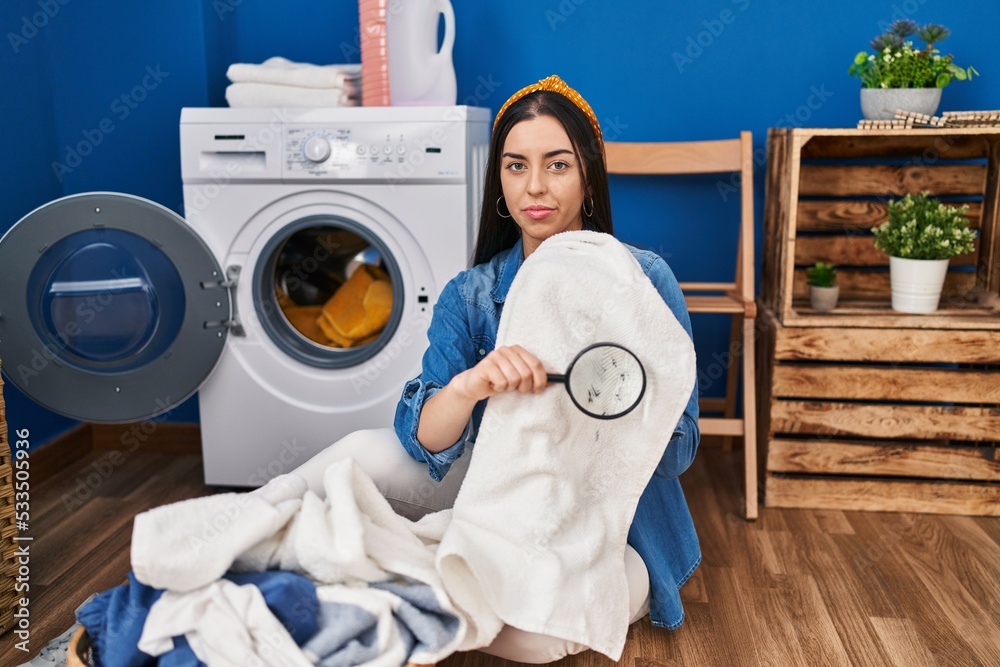 Canvas Prints Hispanic woman holding magnifying glass looking for stain at clothes relaxed with serious expression on face. simple and natural looking at the camera.