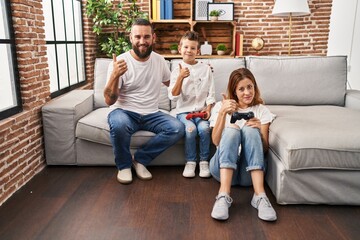 Obraz premium Family of three playing video game sitting on the sofa smiling happy and positive, thumb up doing excellent and approval sign