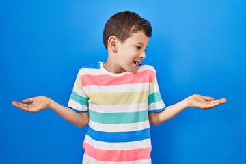 Young caucasian kid standing over blue background smiling showing both hands open palms, presenting...