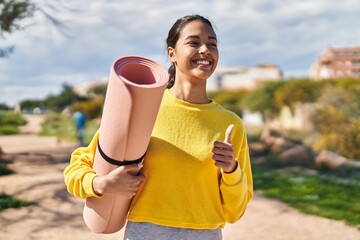 Young african american woman doing ok gesture holding yoga mat at park