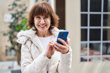 Fototapeta premium Middle age woman smiling confident using smartphone at coffee shop terrace