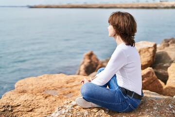 Fototapeta na wymiar Middle age woman smiling confident sitting on the rock at seaside