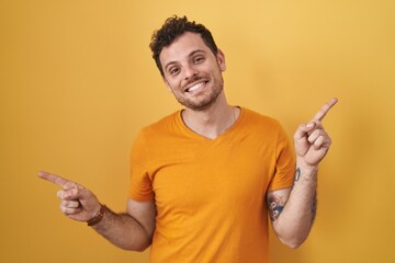 Young hispanic man standing over yellow background smiling confident pointing with fingers to different directions. copy space for advertisement