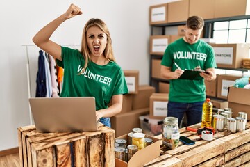 Young woman and man wearing volunteer t shirt at donations stand annoyed and frustrated shouting with anger, yelling crazy with anger and hand raised