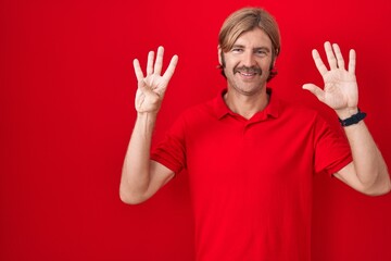 Caucasian man with mustache standing over red background showing and pointing up with fingers...