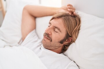 Fototapeta na wymiar Young blond man lying on bed sleeping at bedroom