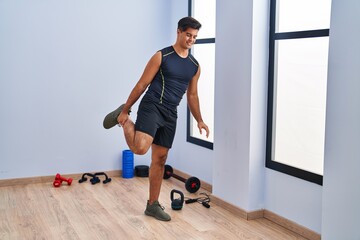 Obraz premium Young hispanic man smiling confident stretching leg at sport center