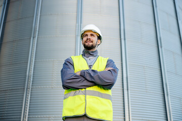 A refinery worker stands outside with arms crossed and smiles in front of the silo.