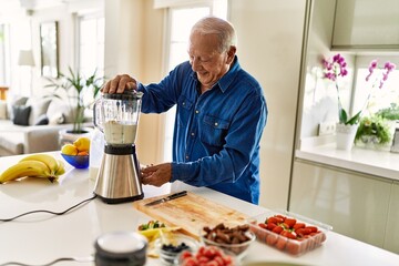 Senior man smiling confident shaking blender at kitchen