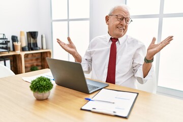 Senior man working at the office using computer laptop smiling showing both hands open palms,...
