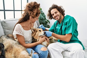 Man and woman wearing veterinarian uniform examining ear dog at home