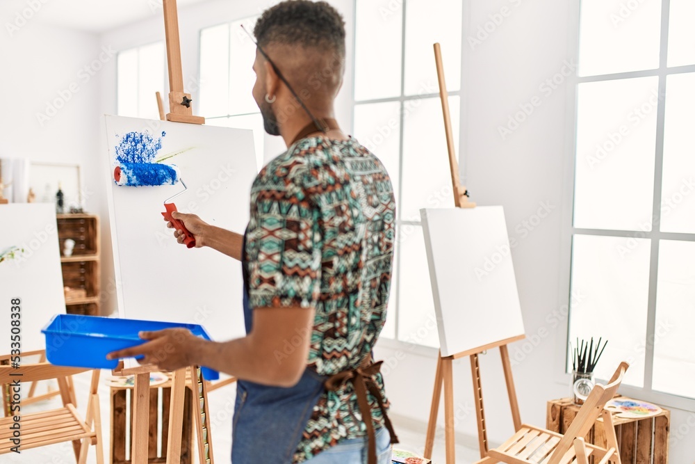 Poster young african american artist man on back view painting with paint roller at art studio.